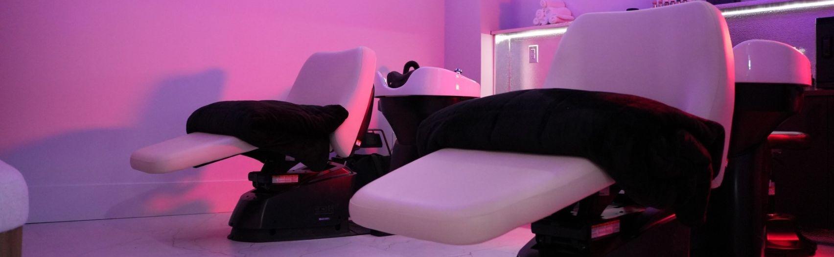 Two reclining wash chairs with white basins in soft pink?purple light, creating a calm modern salon vibe.