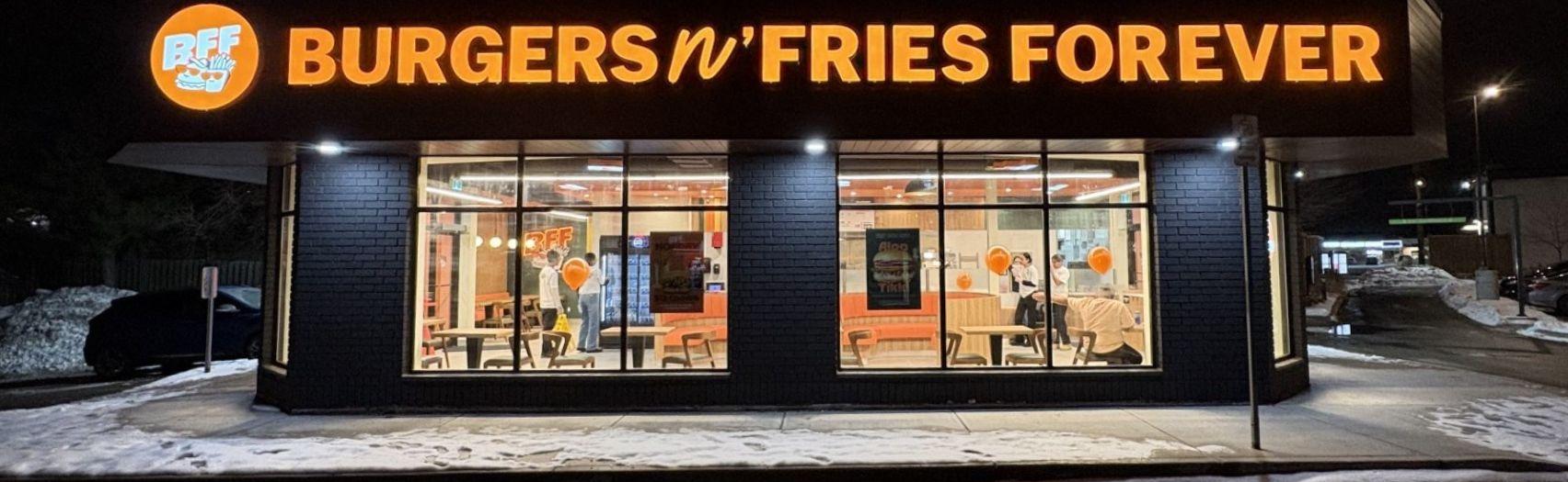 Lit Burgers n’ Fries Forever building glows at night with open sign visible amid snow outside.