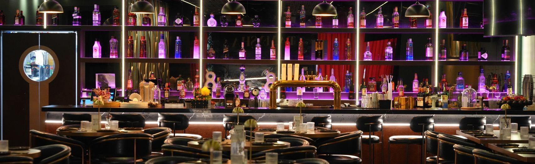 Warm purple and gold bar interior with backlit bottles, pendant lights, and elegant black?gold seating.