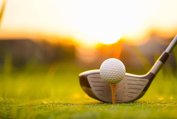 A golf club behind a teed up golf ball outdoors at a gold course