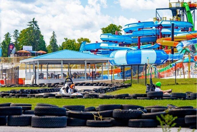Gokarts racing on a track near bright twisting waterslides under a sunny sky with trees around.