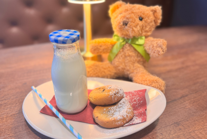 A bottle of milk with a blue checkered lid, two cookies dusted with powdered sugar on a red napkin.