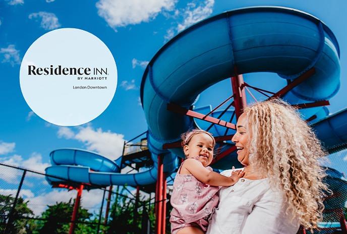 A mother and her young daughter standing in front of a large water park slide in East Park located in London, Ontario