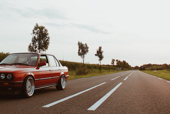 Red vintage car parked on a quiet countryside road lined with trees under a clear sky.
