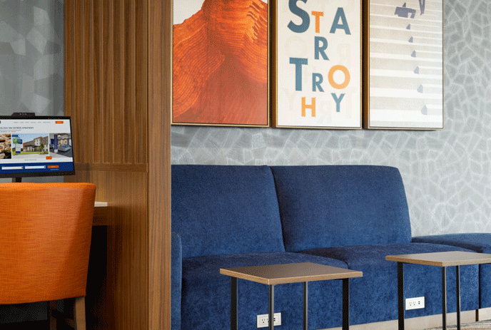Blue couch in a hotel lobby features furniture such as a coffee table, stool, & chair, along with a labtopp