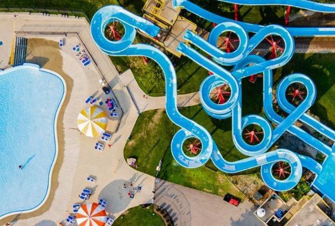 Aerial view of blue water slides twisting above a pool with bright umbrellas and lounge chairs.