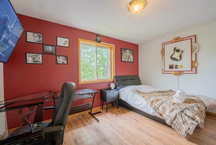 Cozy bedroom with red wall, framed photos, guitar art, fur-covered bed, window view, desk, inviting atmosphere