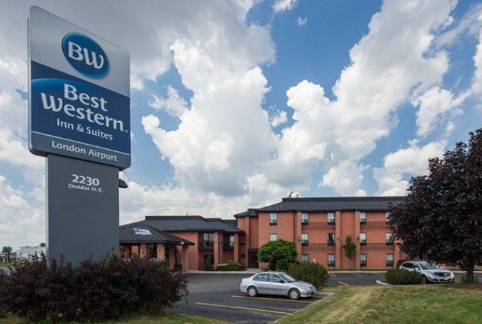 Best Western Inn & Suites London Airport sign, hotel building, parking lot, cars, trees, cloudy sky.
