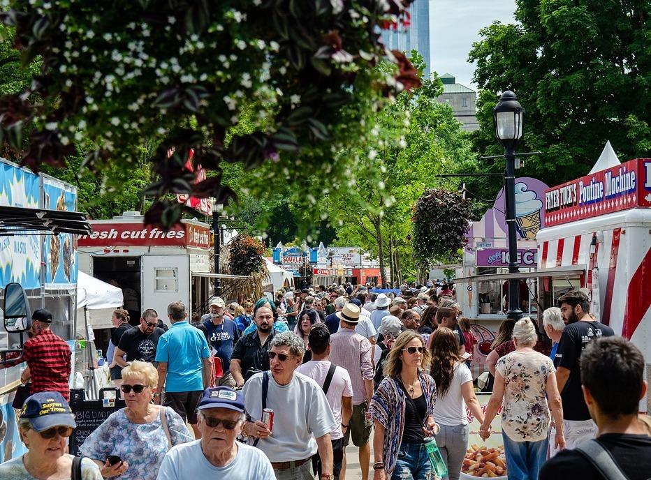 A large crowd of people walking through Victoria Park in London, Ontario during a summer festival