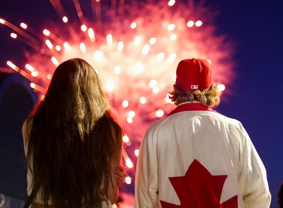 A close up of a young child's hand holding a small flag of Canada in an outdoor festival,