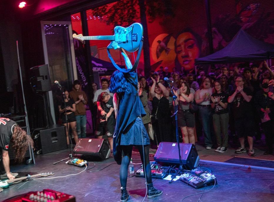 A musician holds up her guitar as a crowd cheers on in excitement during a concert at Market Lane in downtown London, ON