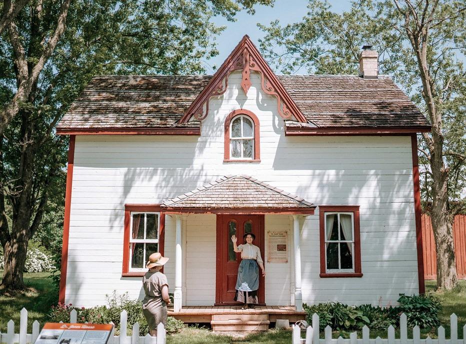 A female standing at the door of an old home waving at Fanashawe Pioneer Village located in London, Ontario