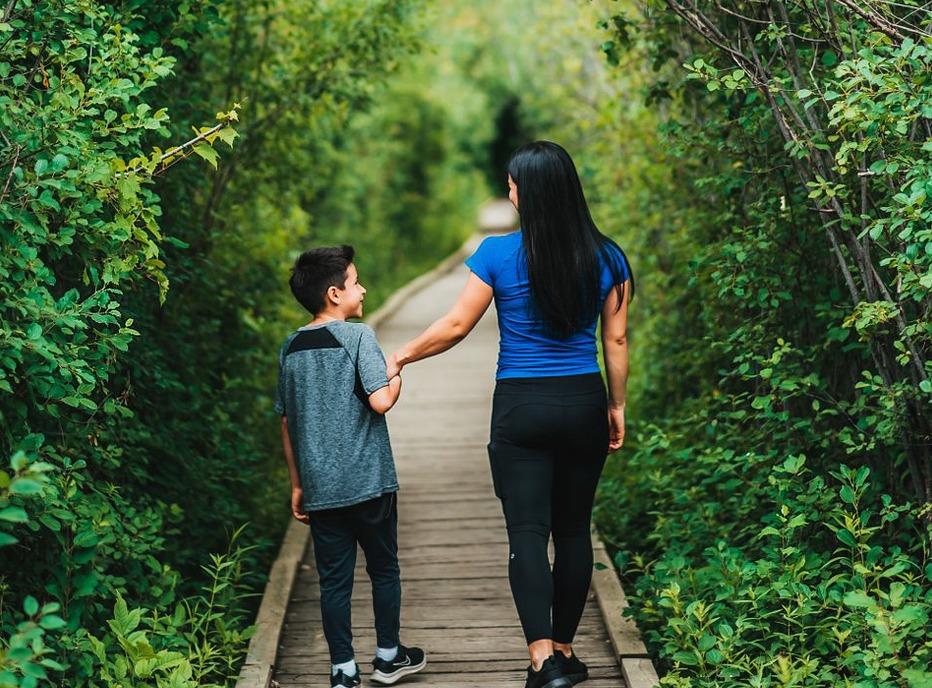 A mother and her son are walking on a wooden path surrounded by trees in Westiminster Ponds located in London, Ontario
