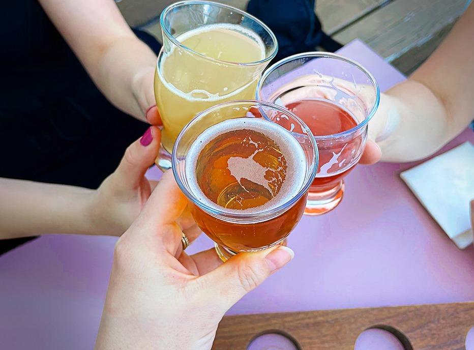 Three hands holding small glasses of craft beer