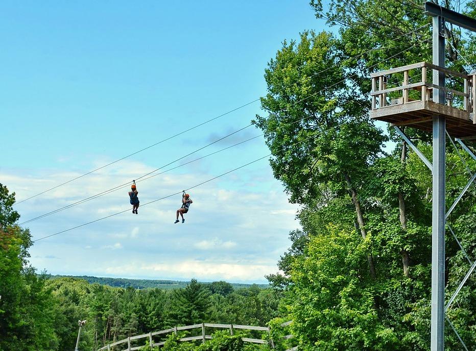 Two people sliding down a zip line with a lush forest in the background at Boler Mountain's Treetop Adventure Park