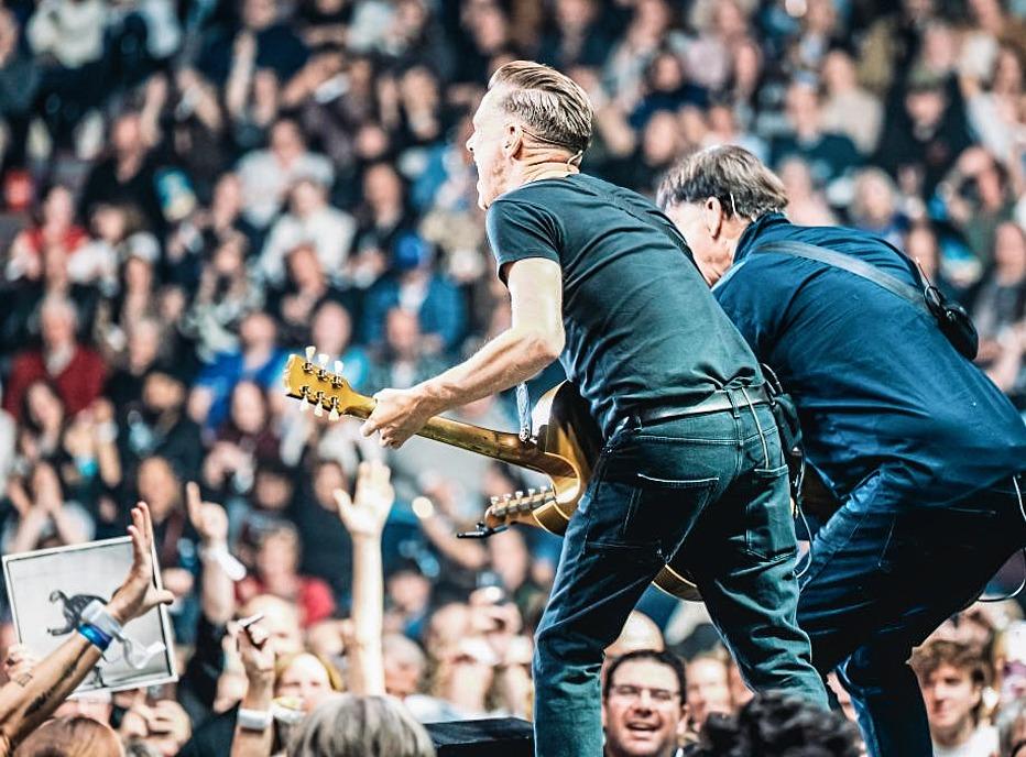 Musician Bryan Adams playing live on stage with a large crowd in the background