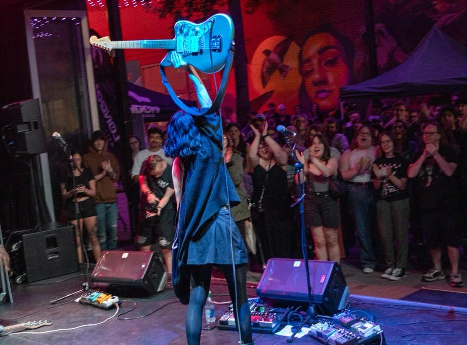 A musician holding up an electric guitar as a crowd cheers on durring a live performance at Dundas Place in London, Ontario