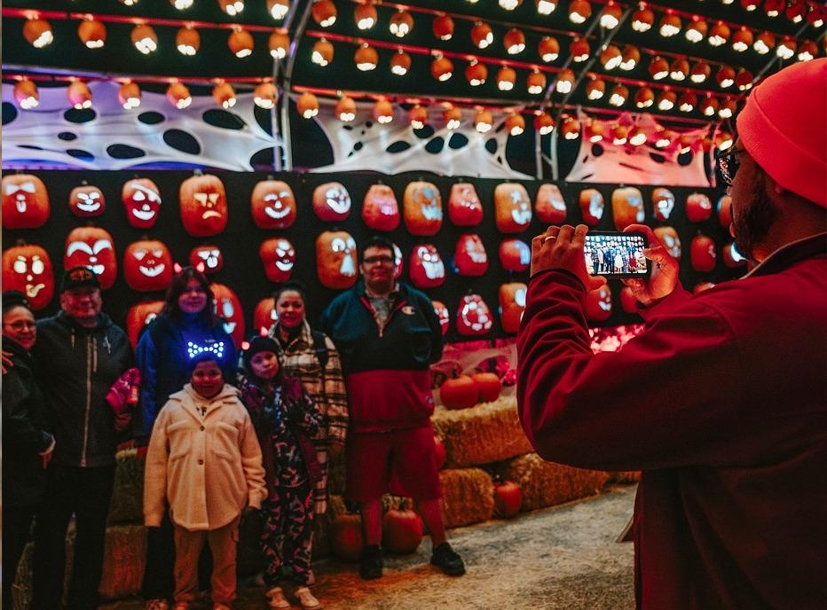 A family gathered for a picture outdoors at night with several carved pumpkins behind them