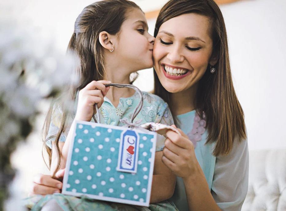 A young girl kissing her mothers cheek while giving her a gift for Mother's Day