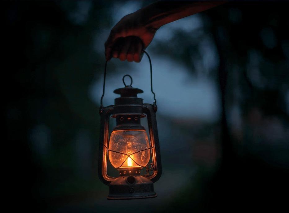 A hand holding a lit lamp at night, mysterious and spooky