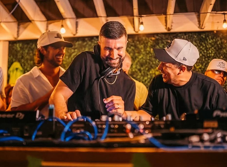 A DJ playing live outdoors with a group of people on stage with him