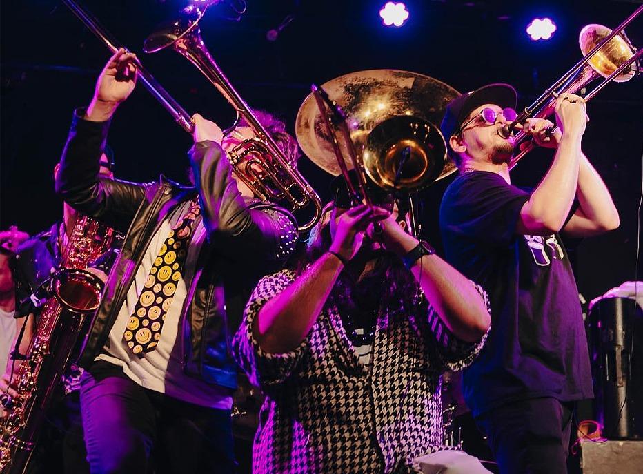 A group of musicians from the band SHOUT!playing trombones and other brass instruments live on stage