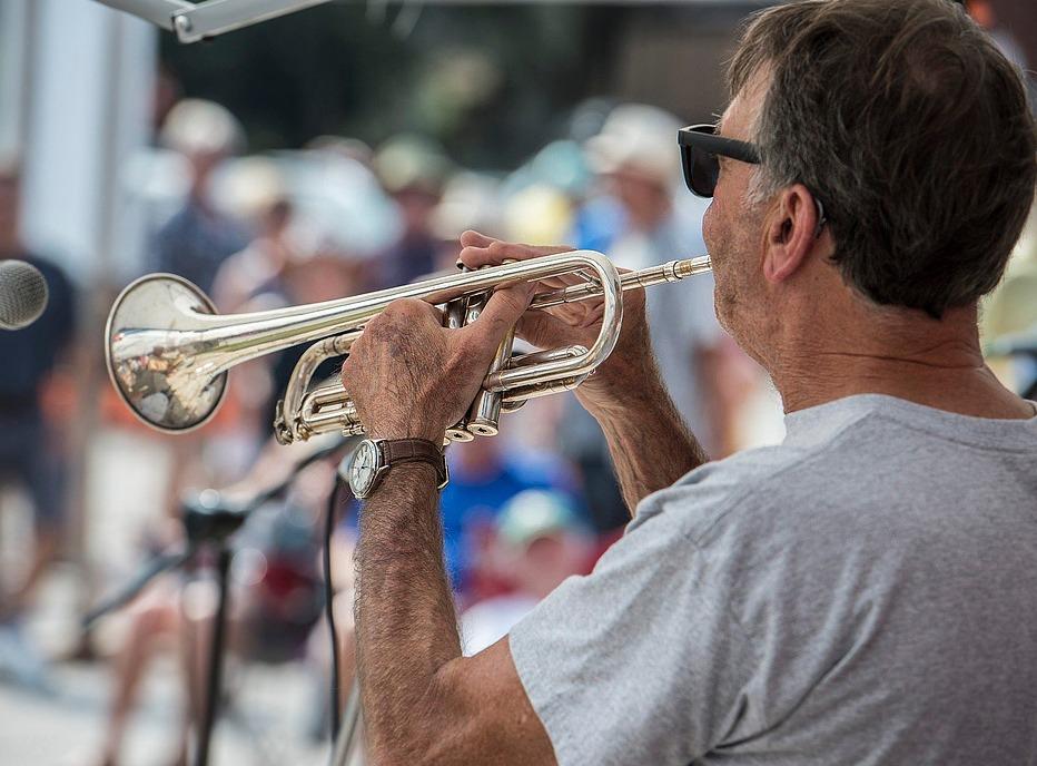 A man playing a trumpet outdoors with a crowd in the background at the Wortley Village Jazz & Blues Festival held in London, ON