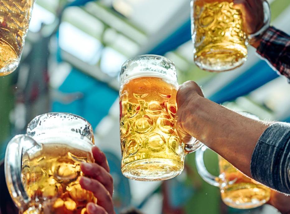 Several people holding up steins of beer outdoors