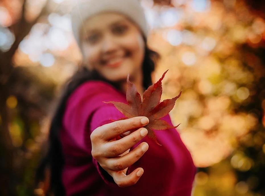 A female holding a maple leaf outdoors during the season of Fall in London, Ontario