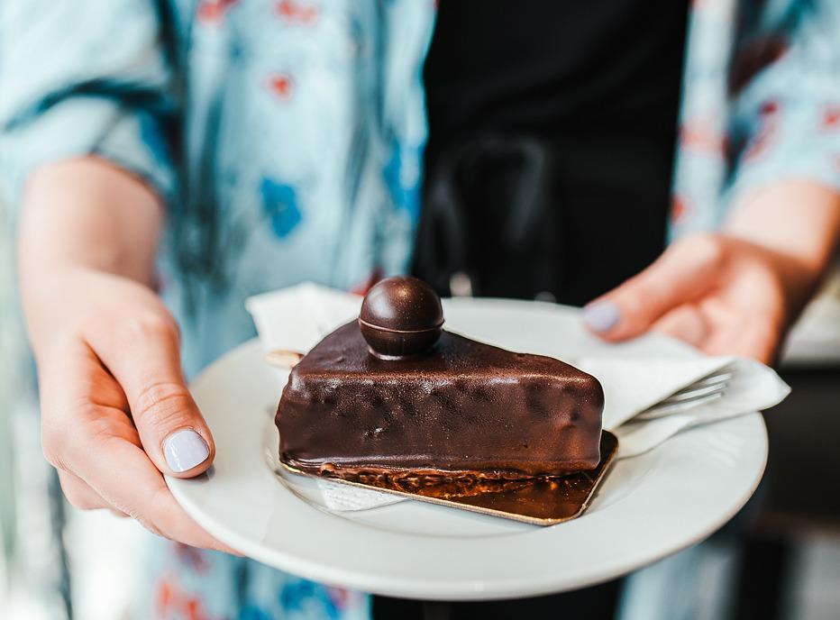 A female holding a plate with a piece of cake covered in chocolate from Happiness Café in London, Ontario