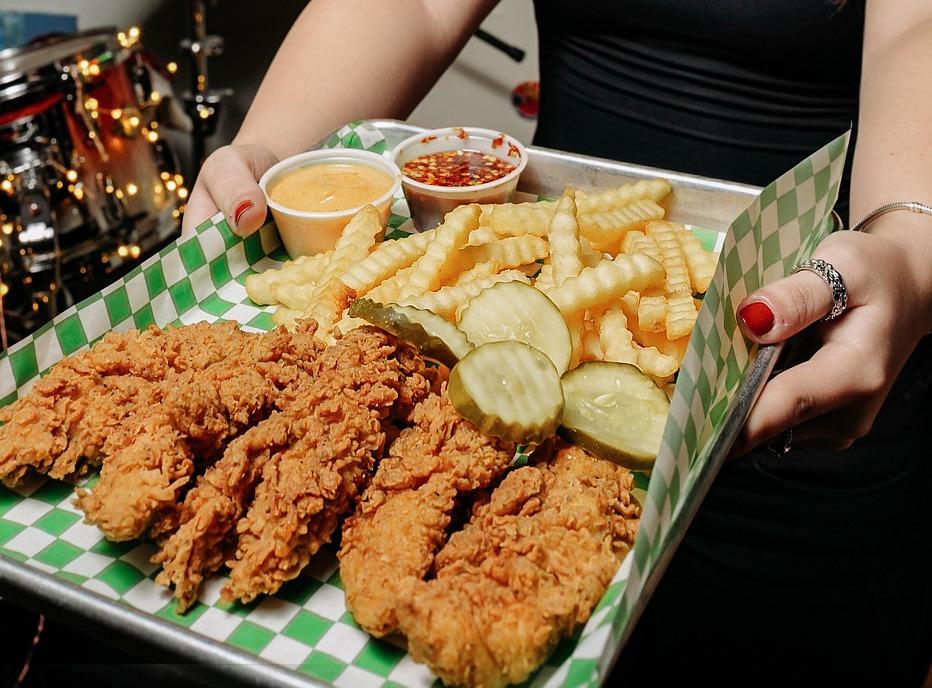 a person carrying a tray of fried chicken strips, waffle french fries and pickels from 808 Chicken House located in London, Ontario