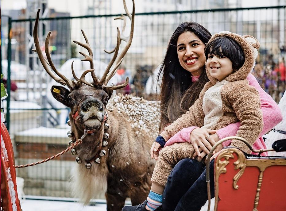 A mother and her young child sitting on Santa's sleigh with a Deer in the background in downtown London, Ontario