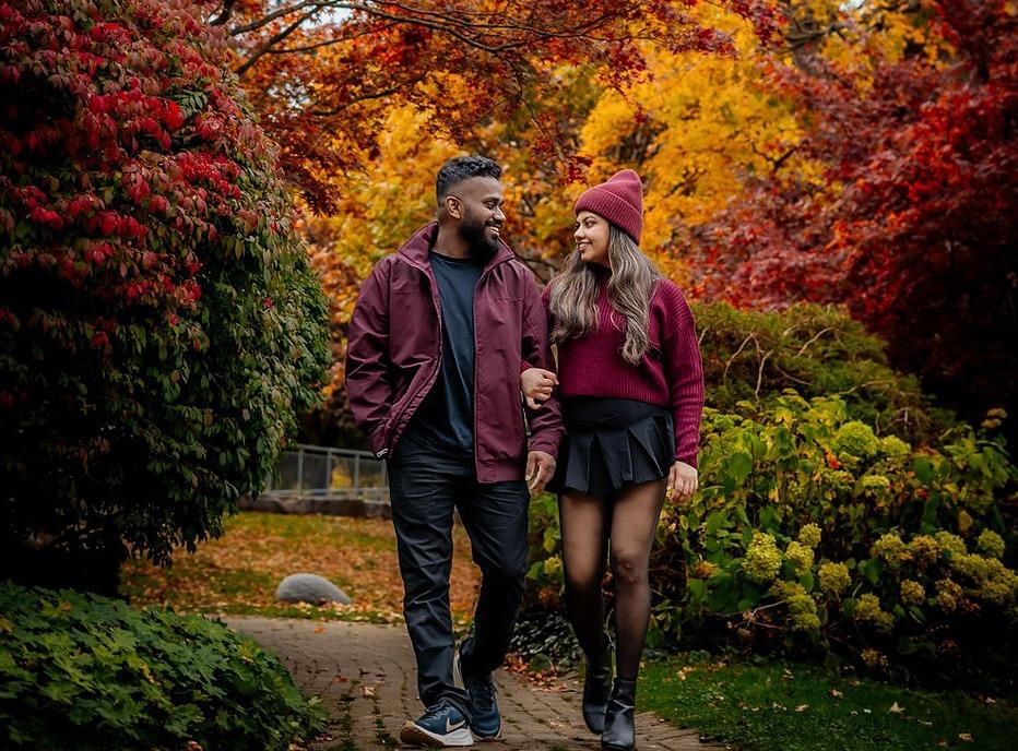 A couple walking on a paved path outdoors with trees and bushes surrounding them in the fall season