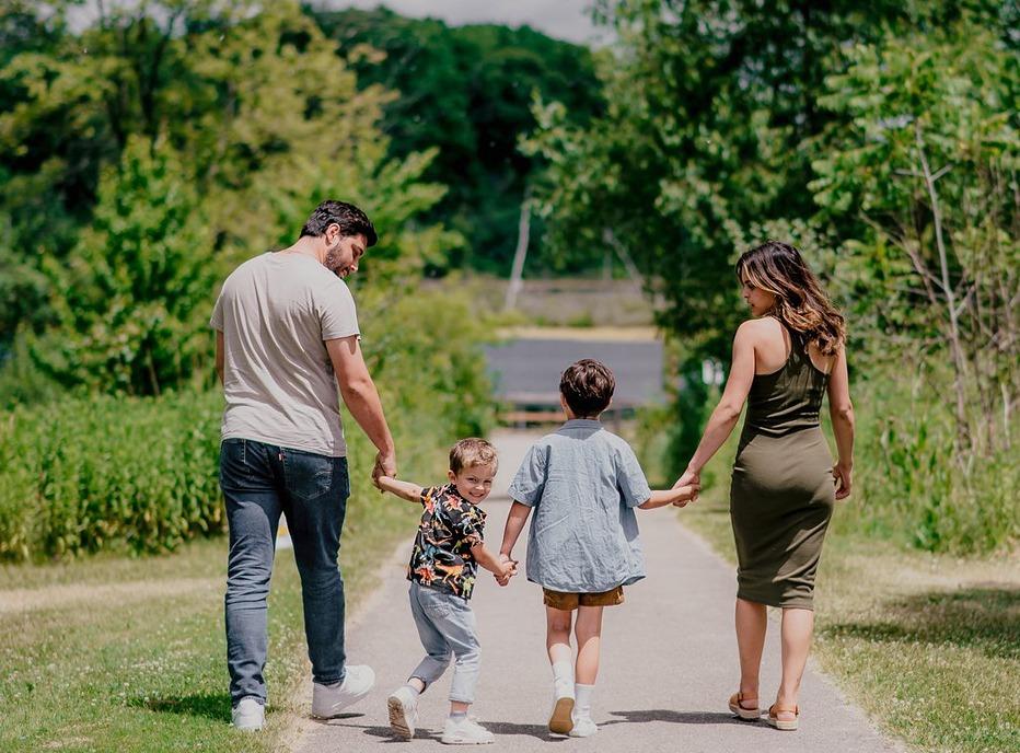 A family walking down a paved path surrounded by large trees in Westminster Ponds located in London, Ontario