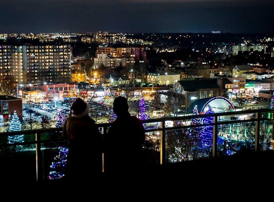 A couple enjoying an overhead view of Victoria Park at night with various trees lit up for the holiday season in London, Ontario