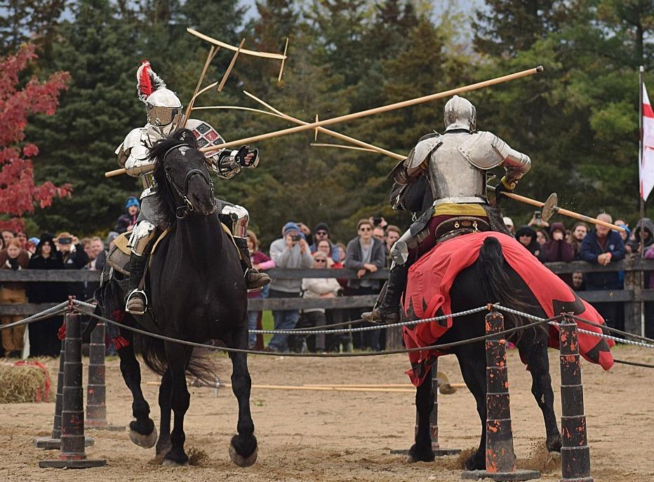 Two knights dressed in armour and riding horses are jousting outdoors at the Oxford Renaissance Festival