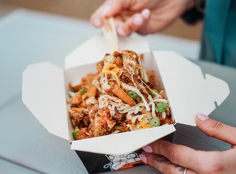 A person eating poutine served in a box