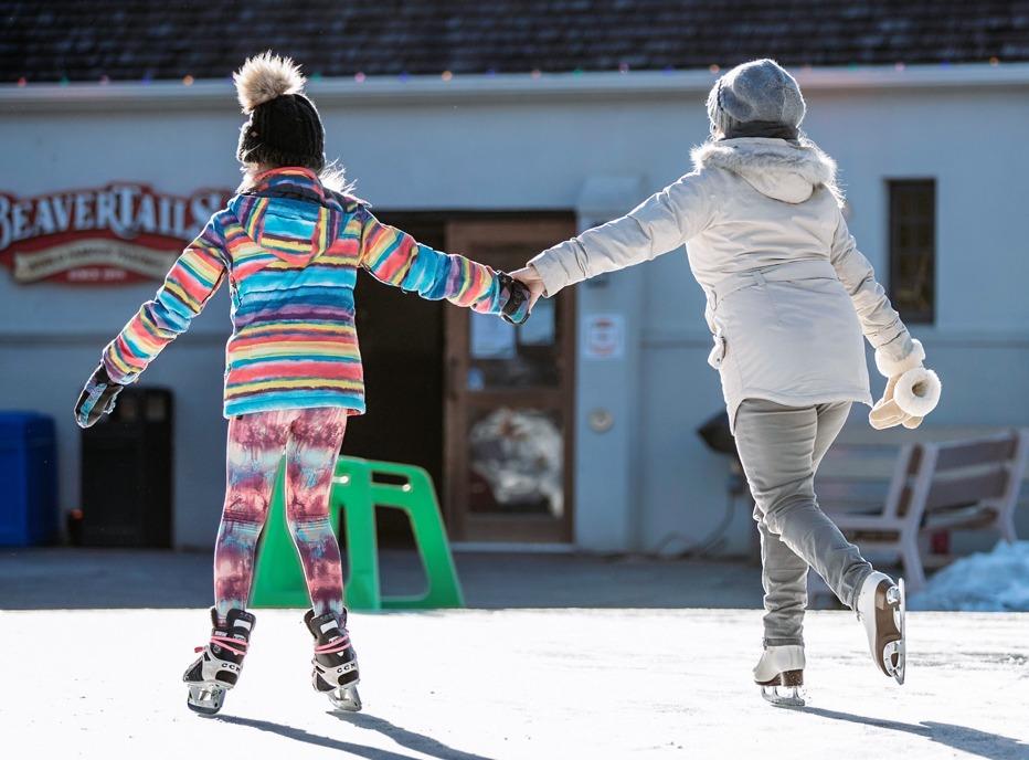 A mother and daughter holding hands and skating outdoors at Storybook Gardens, located in London, Ontario