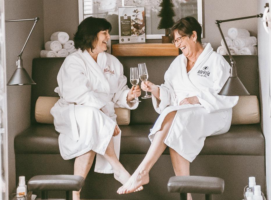 Two women dressed in white robes seated at a the Idlewyd Inn Spa located in London, Ontario