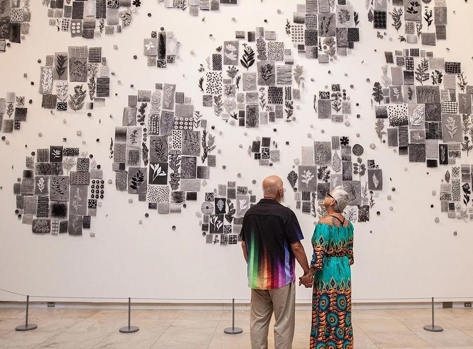 A couple holding hands and looking at a wall with various pieces of artwork on it at Museum London