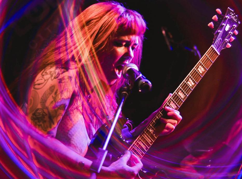 A musician singing and playing her guitar live on stage