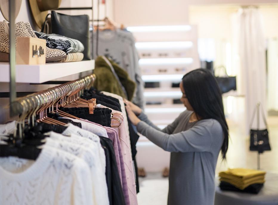 A person looking through various shirts on a rack on display at the store Needs/Wants located in London, Ontario