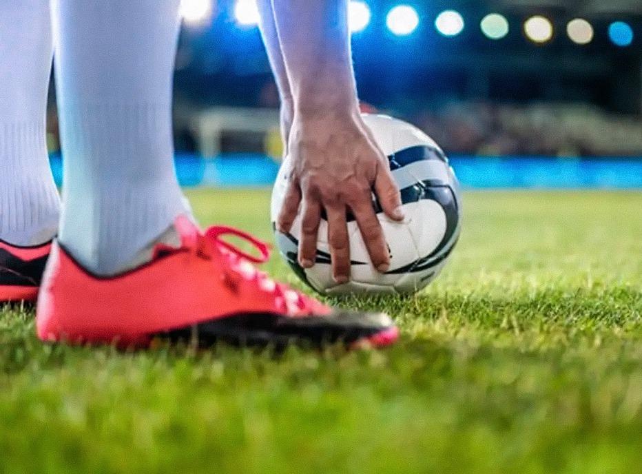 A soccer player placing a ball on the grass in a large stadium