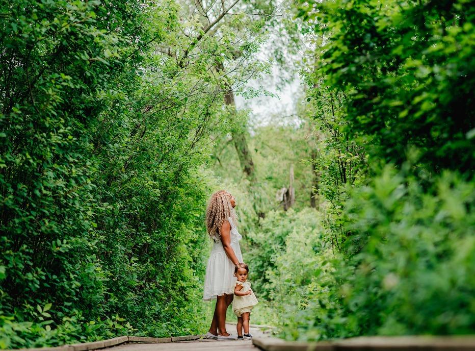 A mother and daughter standing on a path surrounded by large trees in Westminster Ponds located in London, Ontario