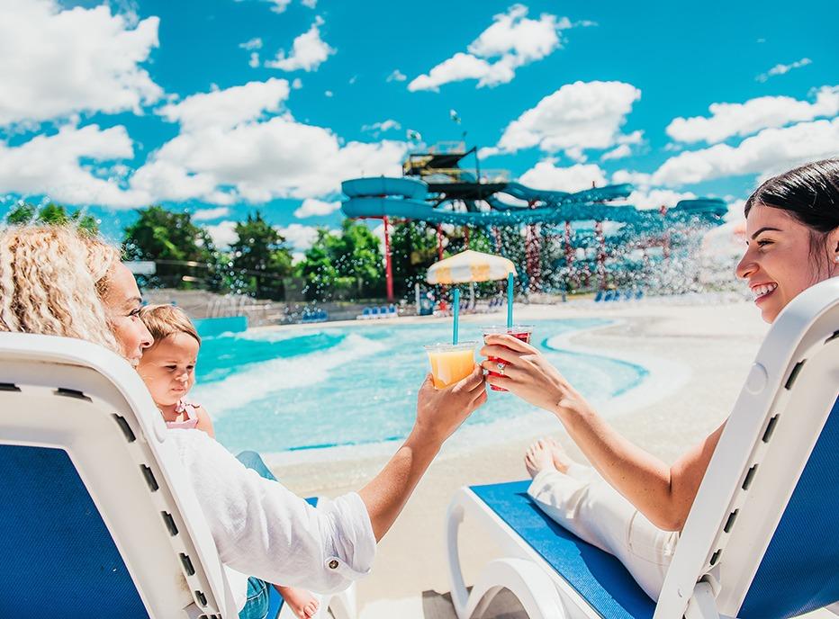 Two females and a young child siting on lounge chairs in  a water park located at East Park in London, Ontario