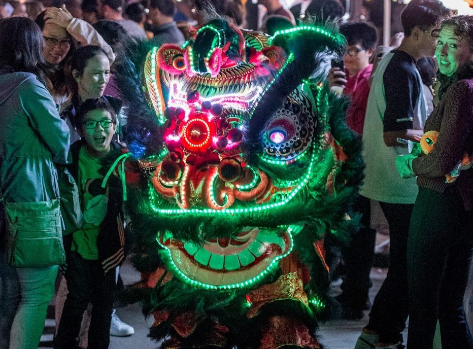 A large group gathered around a traditional dragon costume at the Lucky Lion Night Market