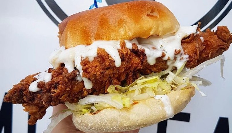 Chicken burger with long chicken strip falling off bun from Kosmos Eatery located in London, Ontario