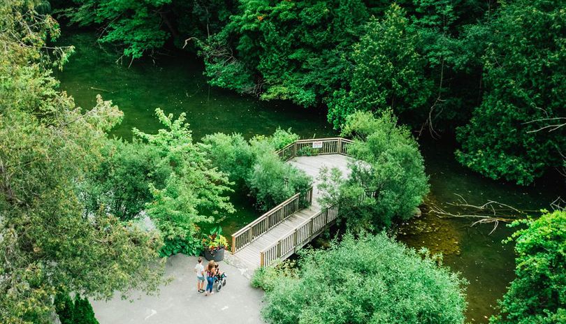 A family with a child in a wheelchair going for a walk on a paved walkway in Springbank Park located in London, Ontario