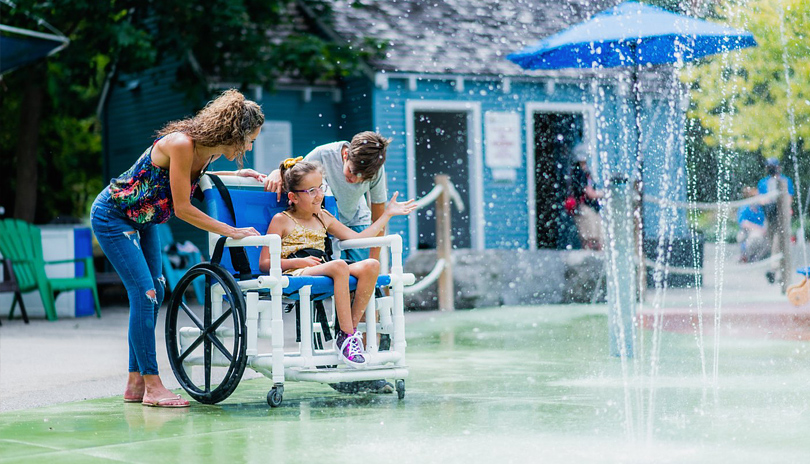 A family with a child in a wheelchair playing in the splash pad at Storybook Gardens located in London, Ontario