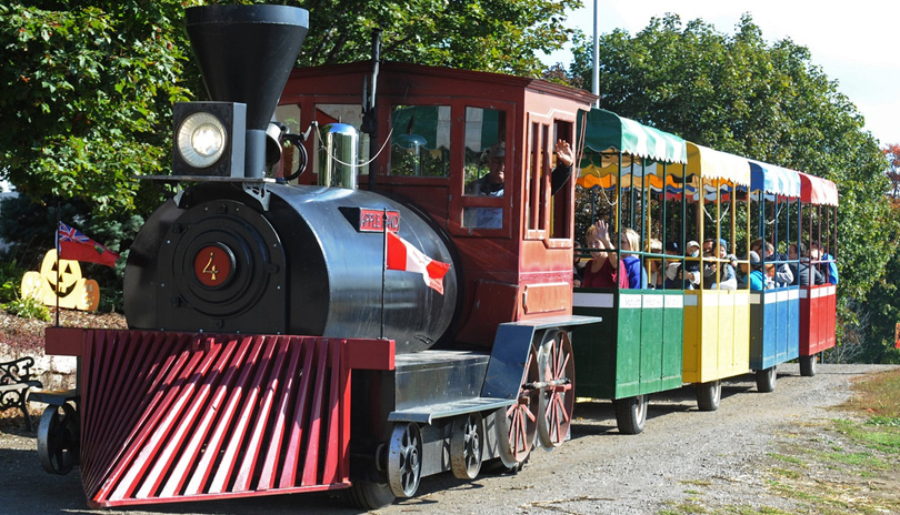 A colourful small train carrying families and children on a dirt path in an apple orchard located at Apple Land Station 
